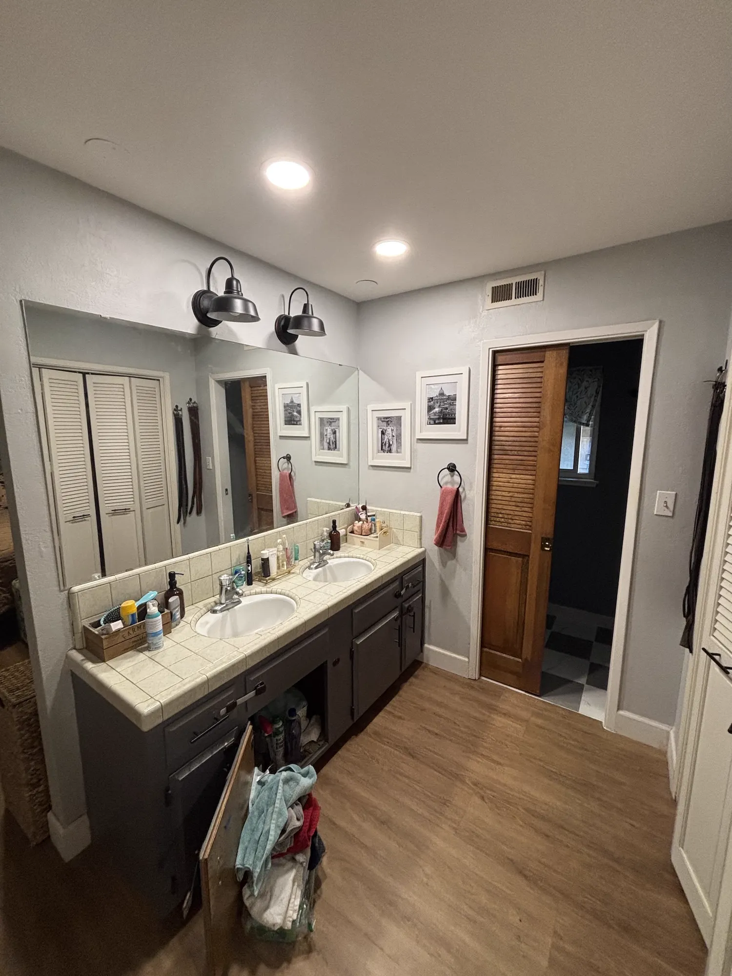 Before: Master bath vanity rebuild: dated tile-top double vanity replaced with a white shaker vanity, quartz counter and backsplash, gold fixtures, and arched mirrors.