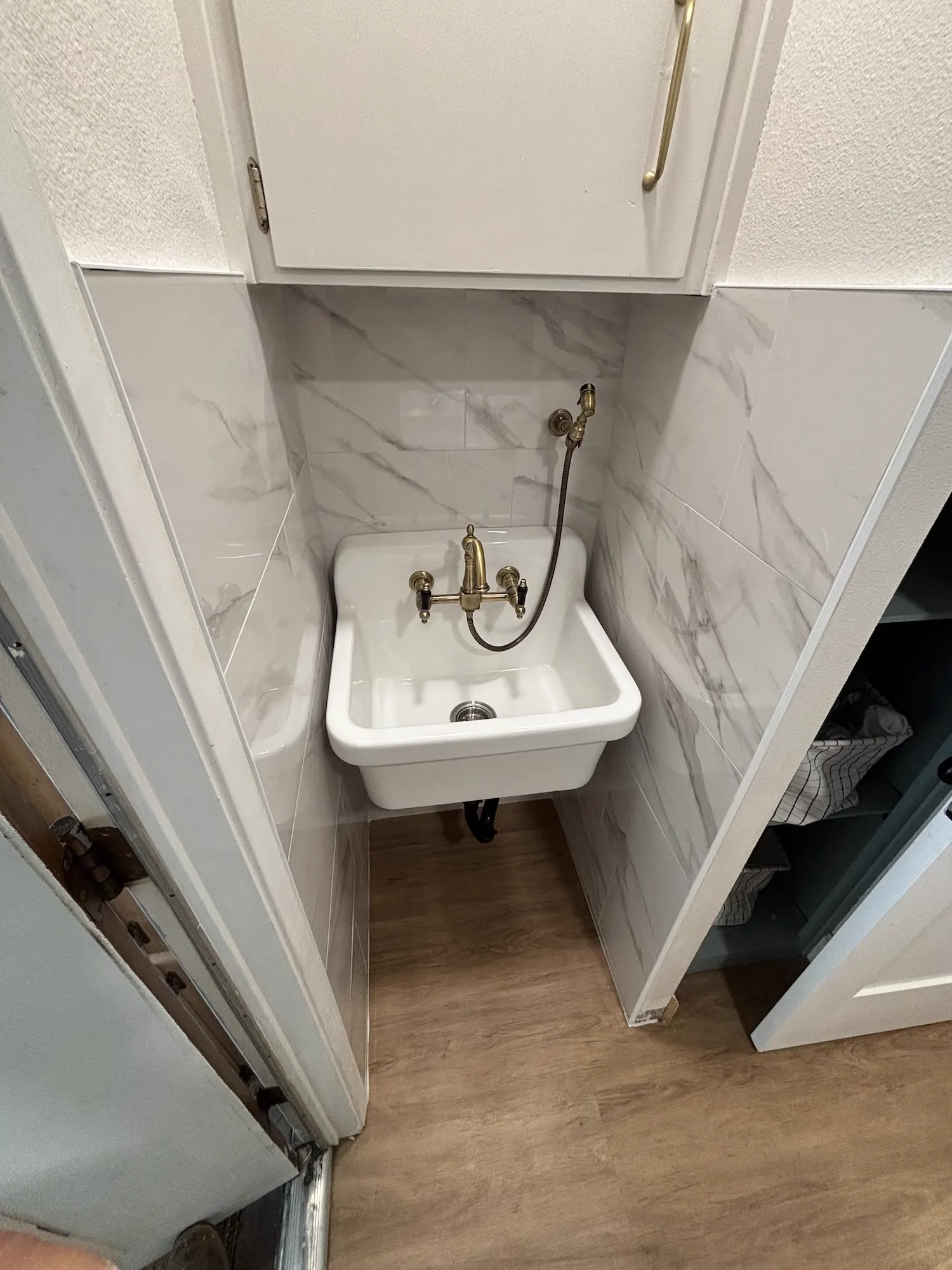 Porcelain wall-mount laundry sink with brass faucet and marble-look tile in a Fresno home
